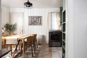 Uma sala de jantar com uma mesa e cadeiras de madeira, um luminário fixado na parede e uma janela com cortinas.