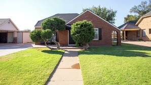 A residential house with a brick exterior, a front yard with a pathway, and two well-maintained trees. - Choosing Texas (Amarillo)