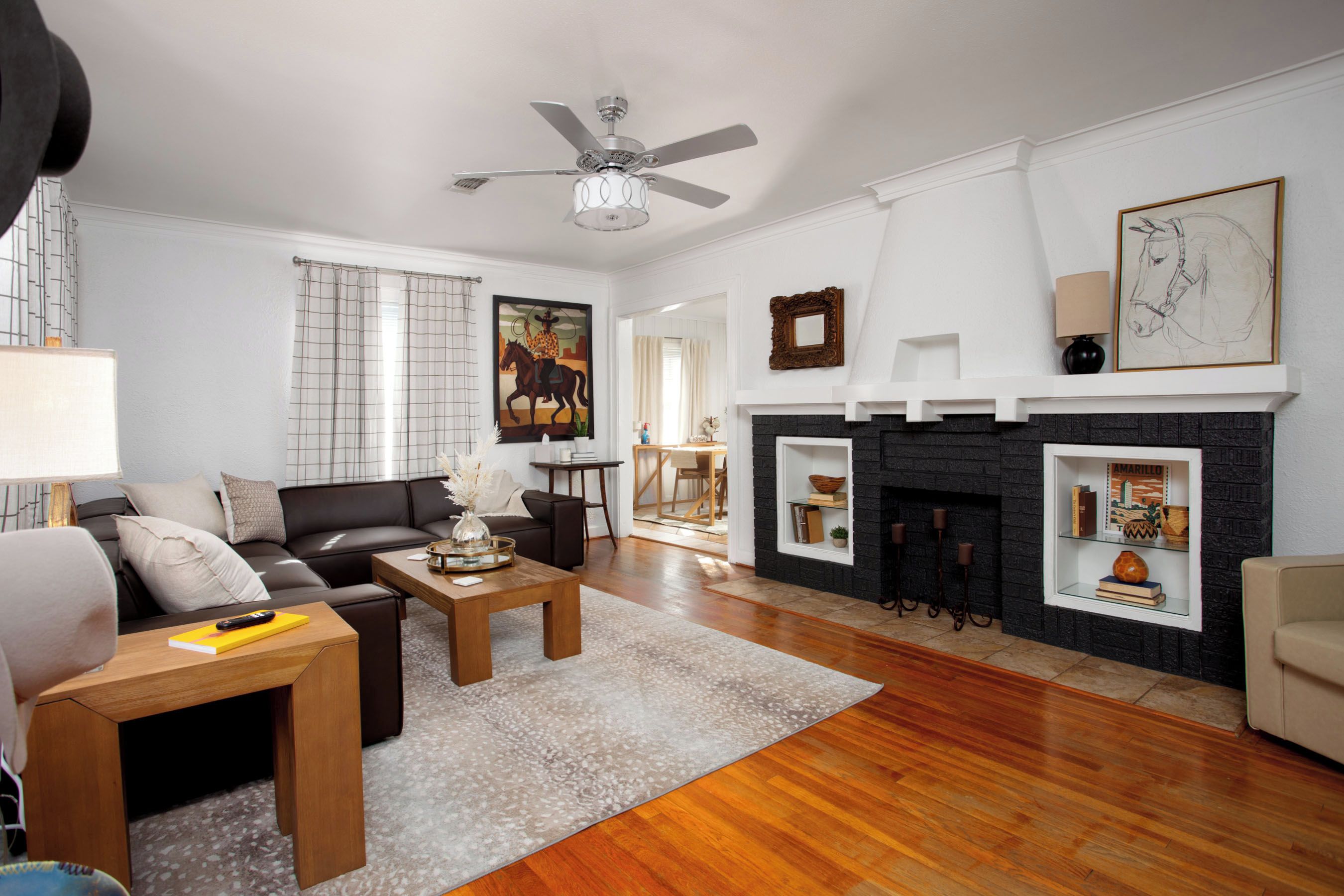 A living room with a fireplace, a ceiling fan, and a painting on the wall.