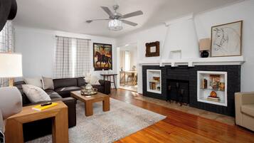 A living room with a fireplace, a ceiling fan, and a painting on the wall.