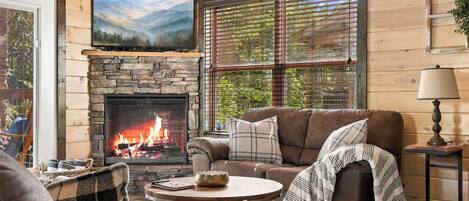 A cozy living room with a stone fireplace, a comfortable sofa, and a television mounted above the fireplace.