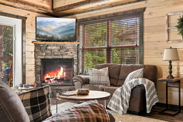 Ein gemütliches Wohnzimmer mit Kamin aus Stein, einer bequemen Couch und einem Fernseher, der über dem Kamin angebracht ist.