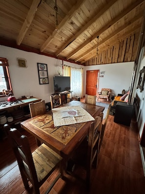 Ein gemütliches Wohnzimmer mit Holzbalkendecke, einem Esstisch mit Stühlen, einem Fernseher und einem Kamin.