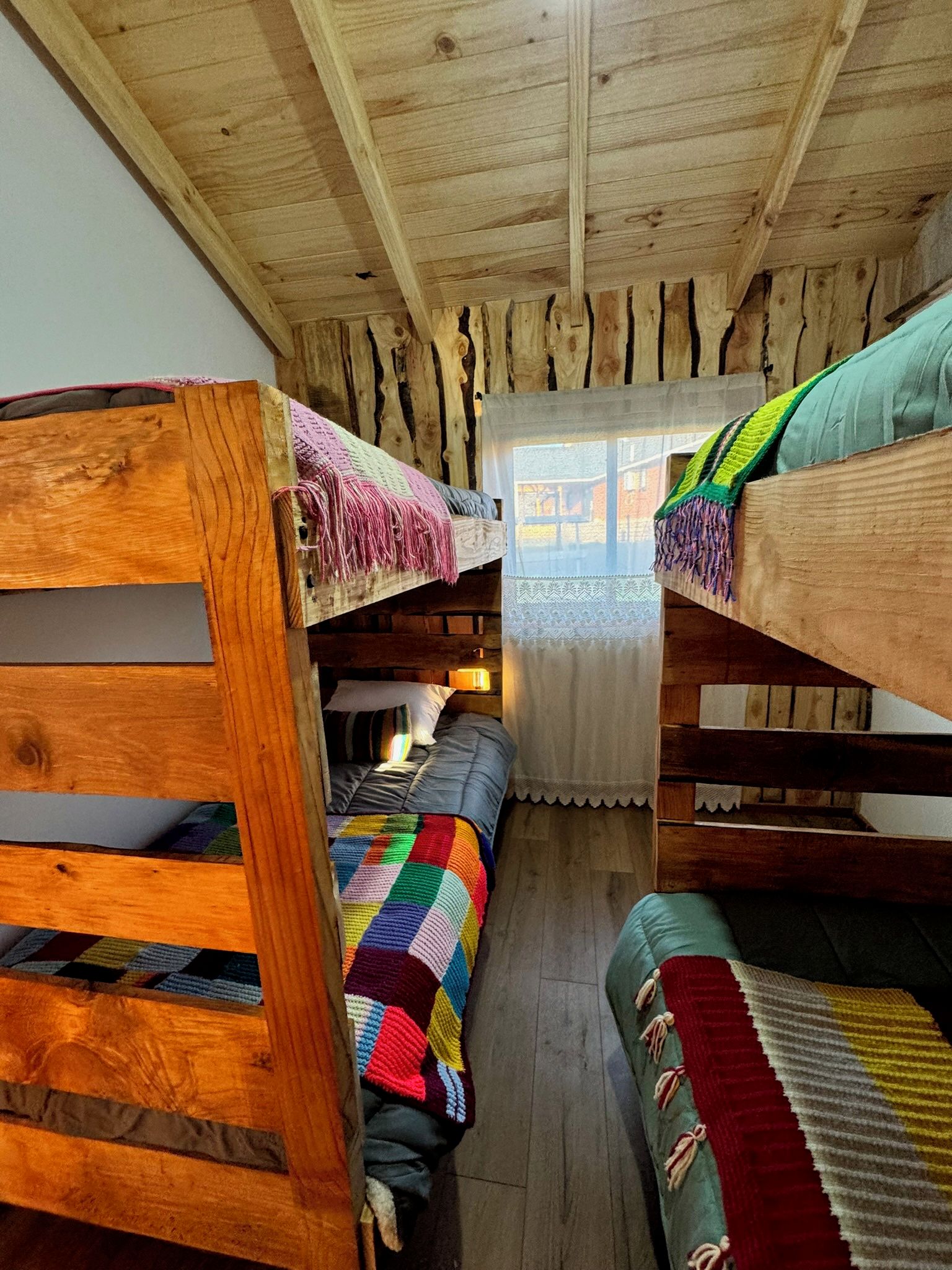 A room with bunk beds, a colorful blanket, and a lace curtain.