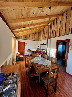 A rustic wooden dining area with a table set for four, a gas stove, and a sewing machine in the background.