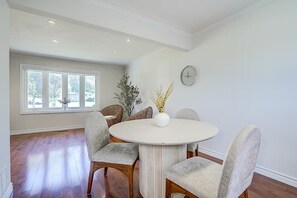 Un coin repas avec une table ronde, quatre chaises, un vase rempli de fleurs jaunes et une horloge au mur.