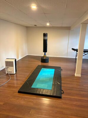 Une pièce avec un plancher en bois, un sac de frappe, un tapis avec du texte et un petit climatiseur.