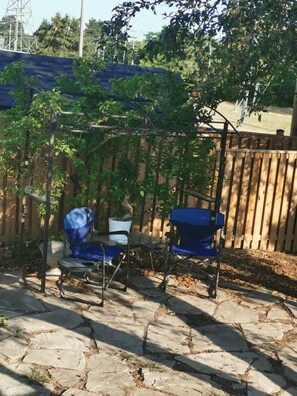 Une terrasse avec deux chaises bleues, une table et une pergola couverte de plantes grimpantes.