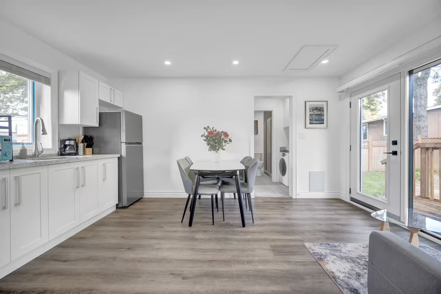 A modern kitchen with white cabinetry, a dining table with chairs, and a large window.