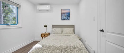 A bedroom with a bed, a nightstand, a window, an air conditioning unit, and a door.