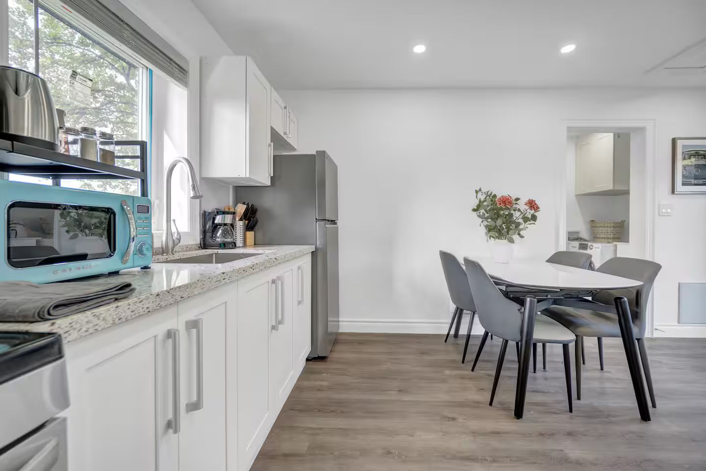 Una cocina moderna con armarios blancos, un microondas azul y una zona de comedor con mesa y sillas.