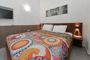 Habitación de hotel con cabecera de madera, cubrecama estampado, televisor de pantalla plana montado en la pared y un cuadro sobre la cama.