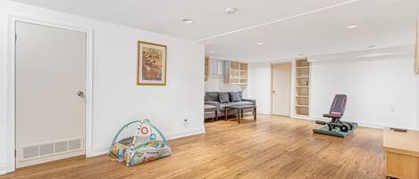 A spacious room with hardwood flooring, a grey sofa, a colorful play tent, and a black exercise bike.