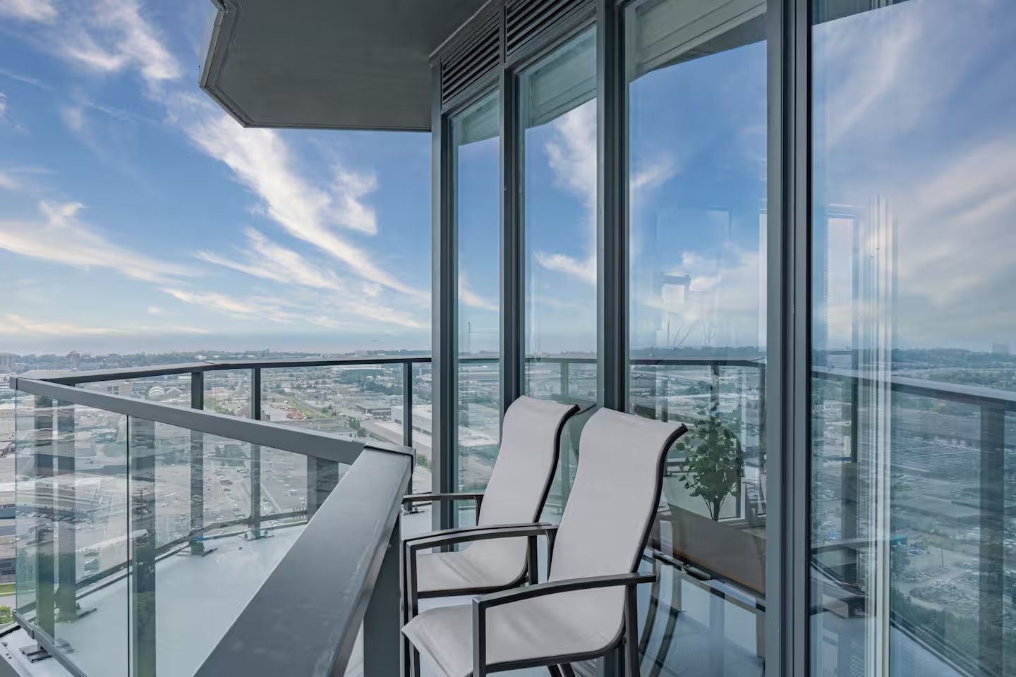 A high-rise balcony with a clear view of the cityscape, a glass railing, and a single chair.