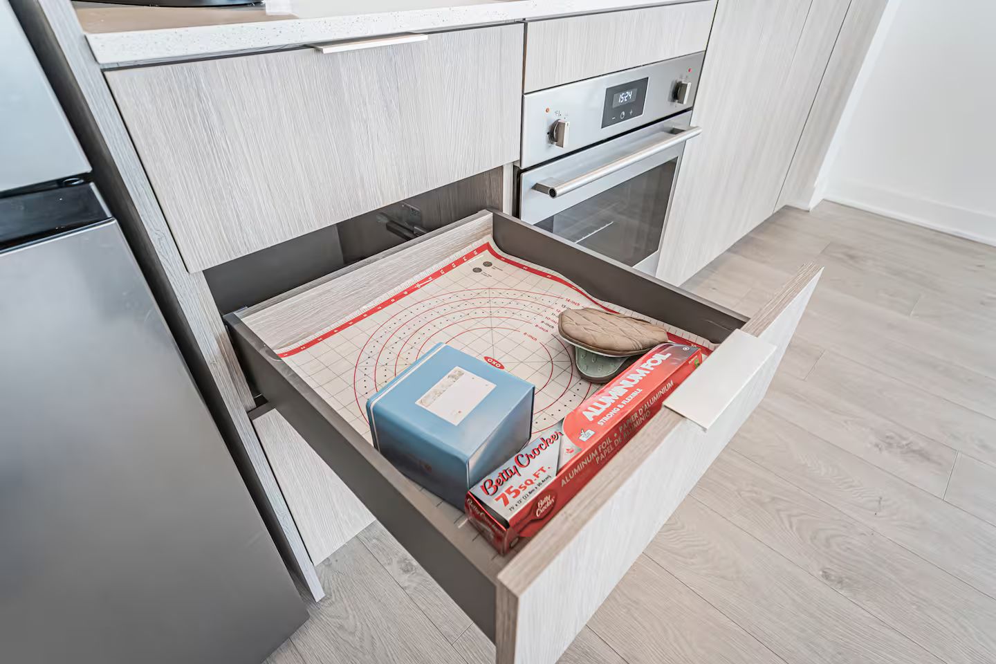 A kitchen with a built-in oven, a stainless steel refrigerator, and a drawer with a cutting mat and baking sheet.