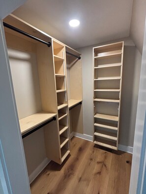 A walk-in closet with open shelving and a rod, wooden flooring, and a ceiling light. - A frame cabin (Swannanoa)