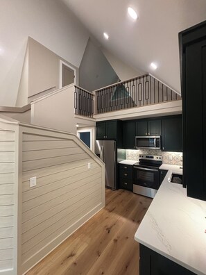 A modern kitchen with a two-tiered balcony, stainless steel appliances, and a wooden floor. - A frame cabin (Swannanoa)