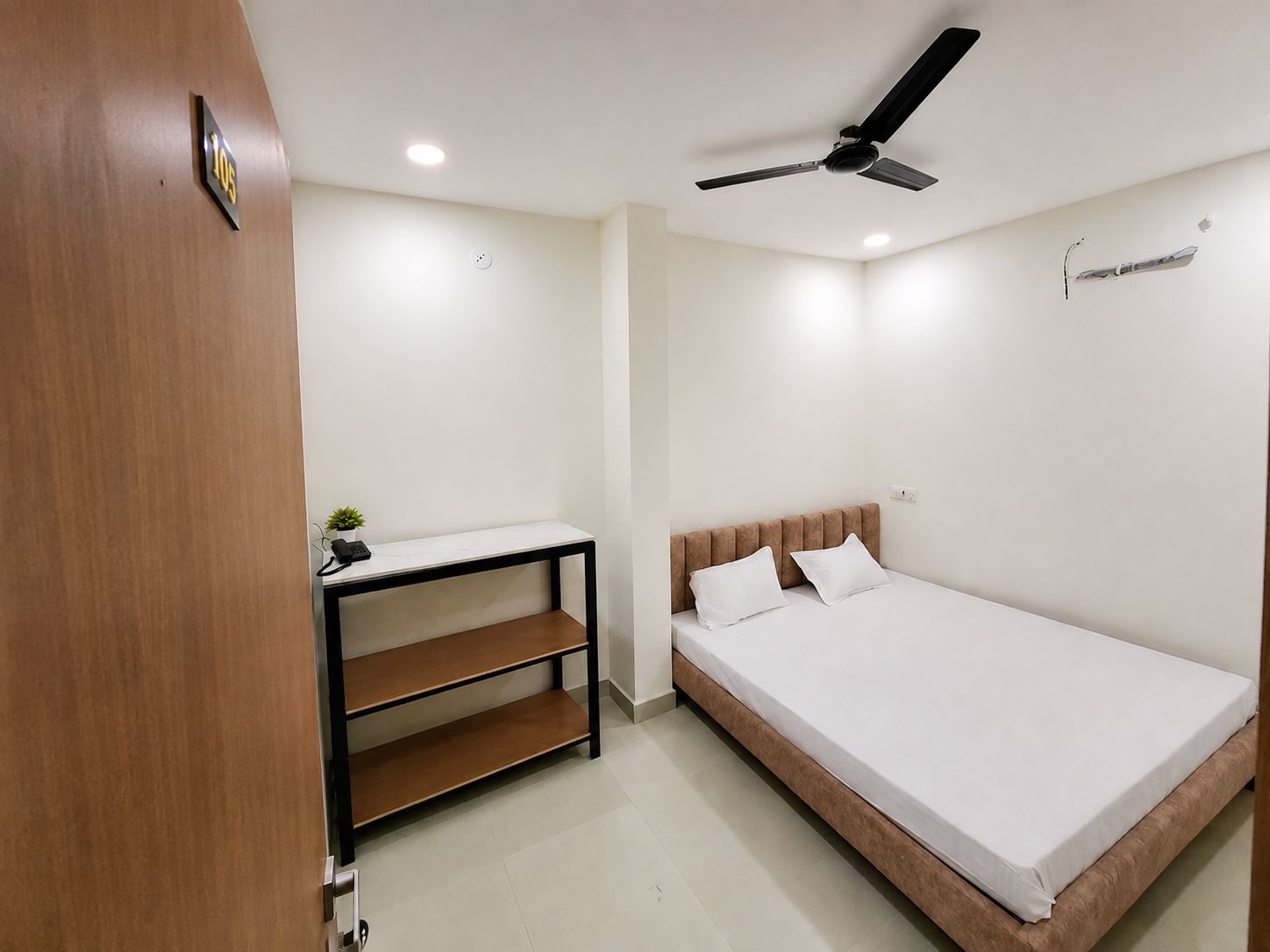 A bedroom with a bed, a desk, a chair, a ceiling fan, and a small plant.