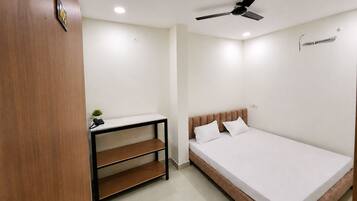 A bedroom with a bed, a desk, a chair, a ceiling fan, and a small plant.