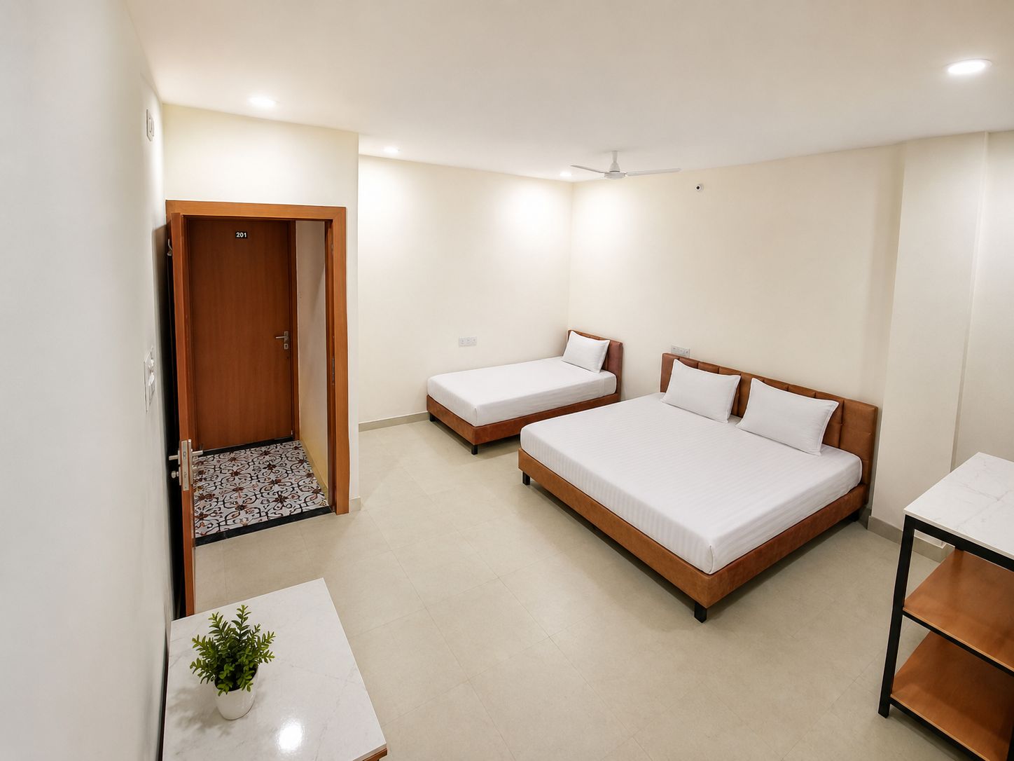 A hotel room with two single beds and one double bed, a small table with a plant, and a door leading to another room.