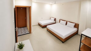 Een hotelkamer met twee eenpersoonsbedden en een ruim bed, een kleintje tafeltje met een plant, en een deur naar een gang.