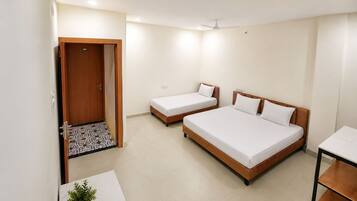 A hotel room with two single beds and one double bed, a small table with a plant, and a door leading to another room.