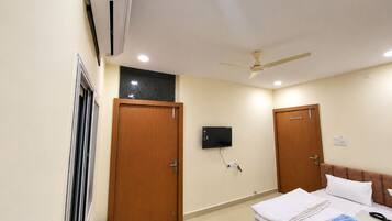 A hotel room with a bed, a ceiling fan, an air conditioning unit, and a television mounted on the wall.