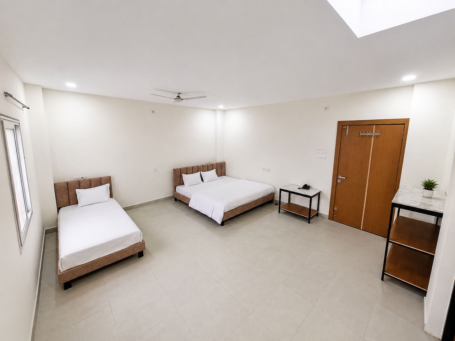 A hotel room with two beds, a desk, a wardrobe, and a ceiling fan.