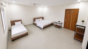 Een hotelkamer met twee bedden, een klein tafeltje, een kledingkast en een plafondventilator.