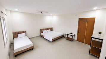 A hotel room with two beds, a desk, a wardrobe, and a ceiling fan.