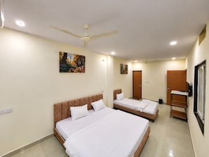 A hotel room with two beds, a ceiling fan, and artwork on the walls. - HOTEL SHREE MANGLA (Ujjain)