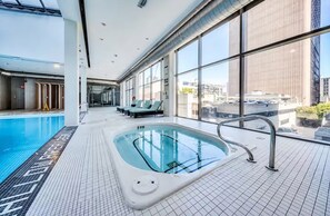 Ein moderner, überdachter Pool mit Glaswänden, Fliesenboden und Blick auf die Stadt.