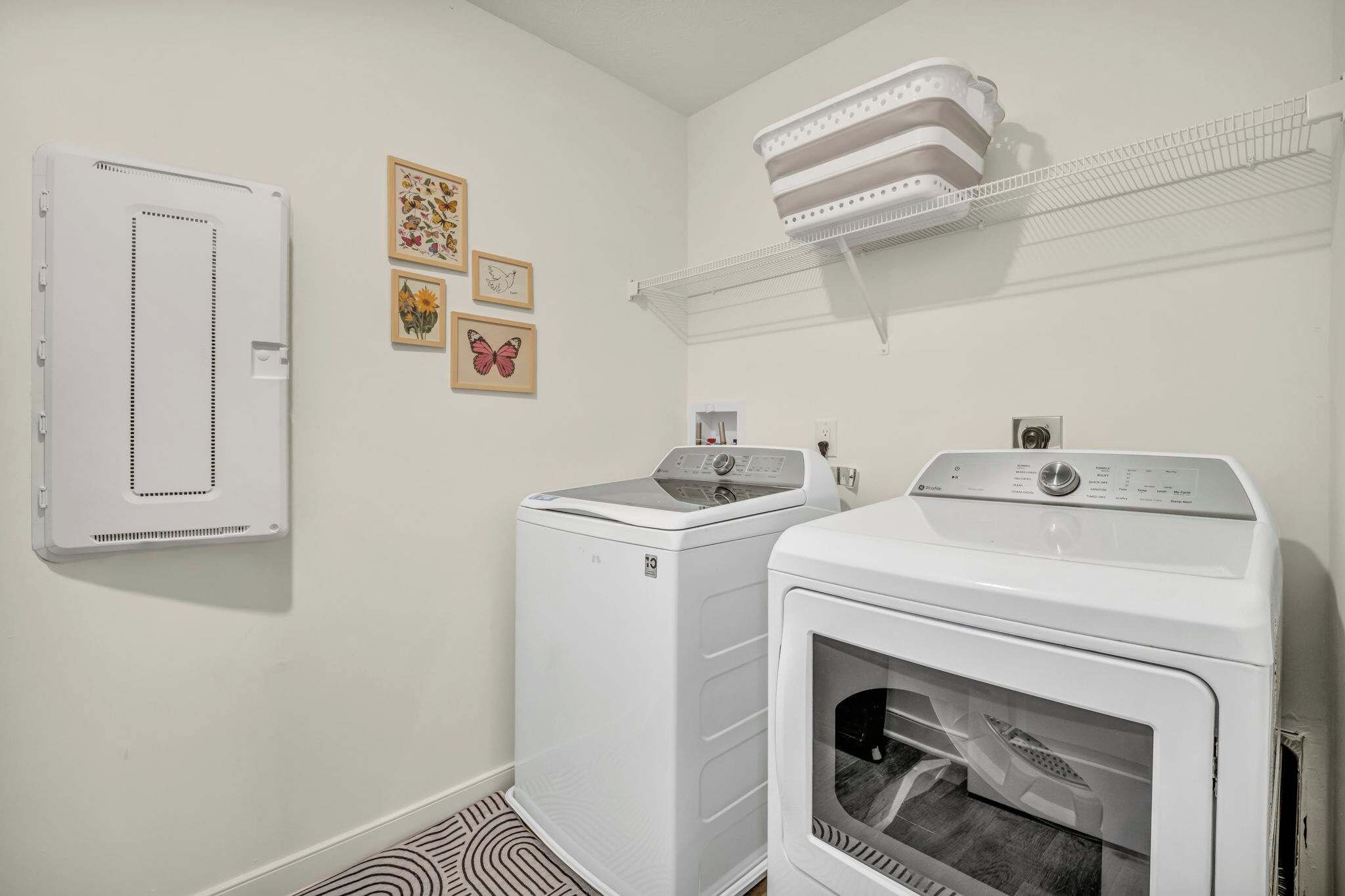 A laundry room with a wall-mounted dryer, a stacked washer-dryer unit, and a shelf above the dryer.