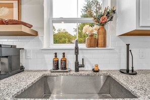 A kitchen with a granite countertop, a stainless steel sink, a modern faucet, and a window with a view of trees. - Arcade | Foosball | Fire Table Patio | West Akron (Akron)