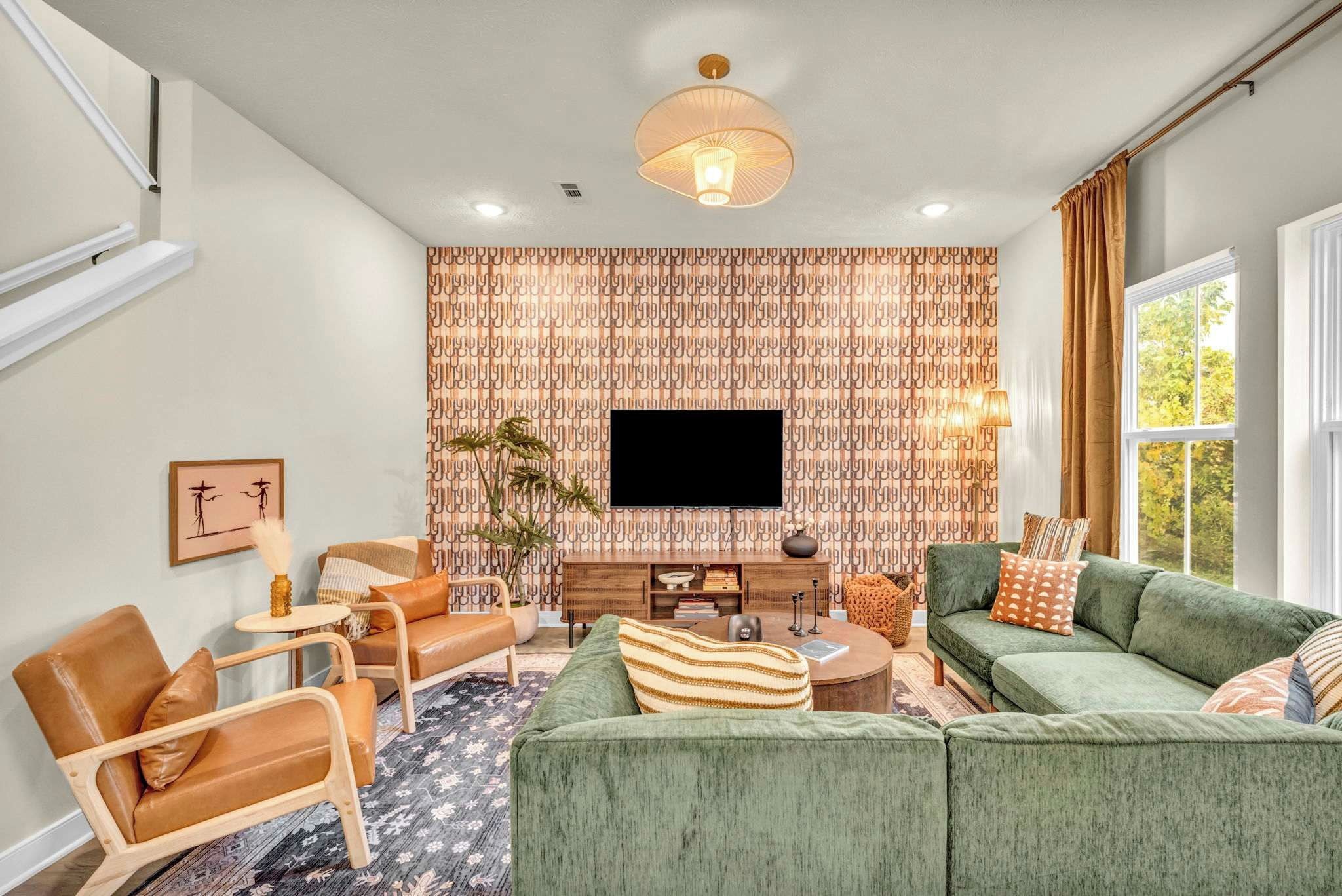 A modern living room with a flat-screen TV, a green sofa, a brown leather chair, and a patterned wall.