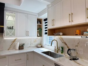 Une cuisine moderne avec des meubles blancs, un plan de travail en marbre, un évier et une machine à café.