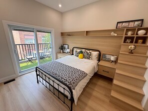 Une chambre à coucher comprenant un lit, une table de chevet, une étagère avec des objets décoratifs et une vue sur l’extérieur.