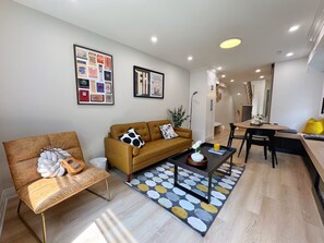 Ein modernes Wohnzimmer mit einer Couch, einem Couchtisch und einem Sessel. Es gibt einen Essbereich mit Tisch und Stühlen.
