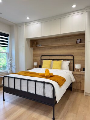 Ein Schlafzimmer mit einem Bett, Nachttischen, einem Beistelltisch, einem Holz-Kopfteil und einem Fenster mit Jalousien.