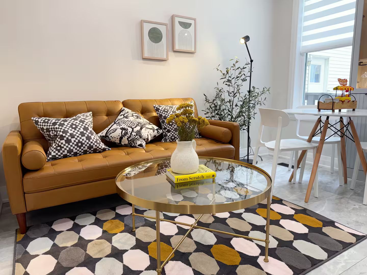 A modern living room with a brown leather sofa, patterned cushions, a glass coffee table, and a hexagonal patterned rug.
