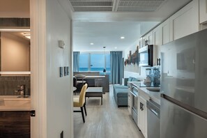 A modern kitchen with stainless steel appliances, a dining area with a view, and a living space with a sofa and a TV. - Myrtle Beach Oceanfront Escape at Yachtsman S1004 (Myrtle Beach)