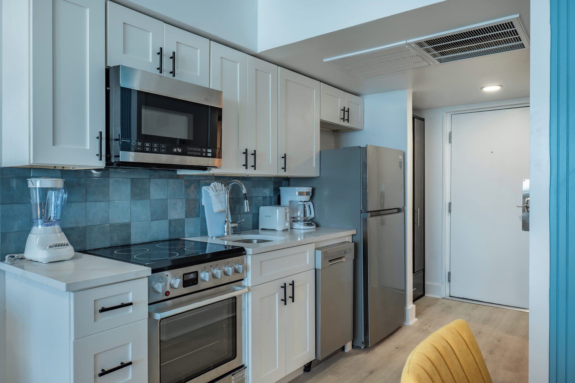 A modern kitchen with white cabinets, a microwave, a stove, a coffee maker, and a refrigerator.
