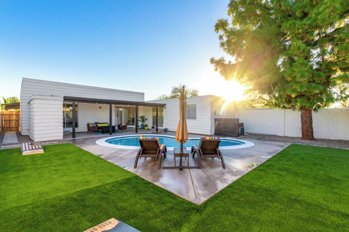A modern house with a backyard featuring a swimming pool, a covered patio, and a well-maintained lawn.