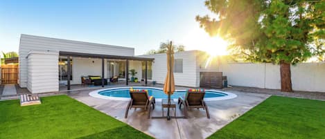 A modern house with a backyard featuring a swimming pool, a covered patio, and a well-maintained lawn.