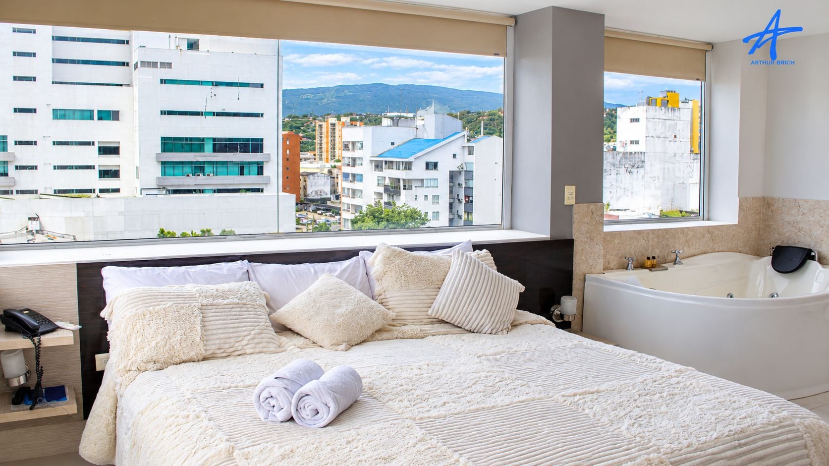 Una habitación de hotel con una cama grande, una bañera y vistas a la ciudad.