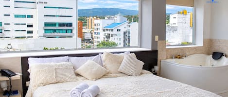 A hotel room with a large bed, a bathtub, and a view of the cityscape.