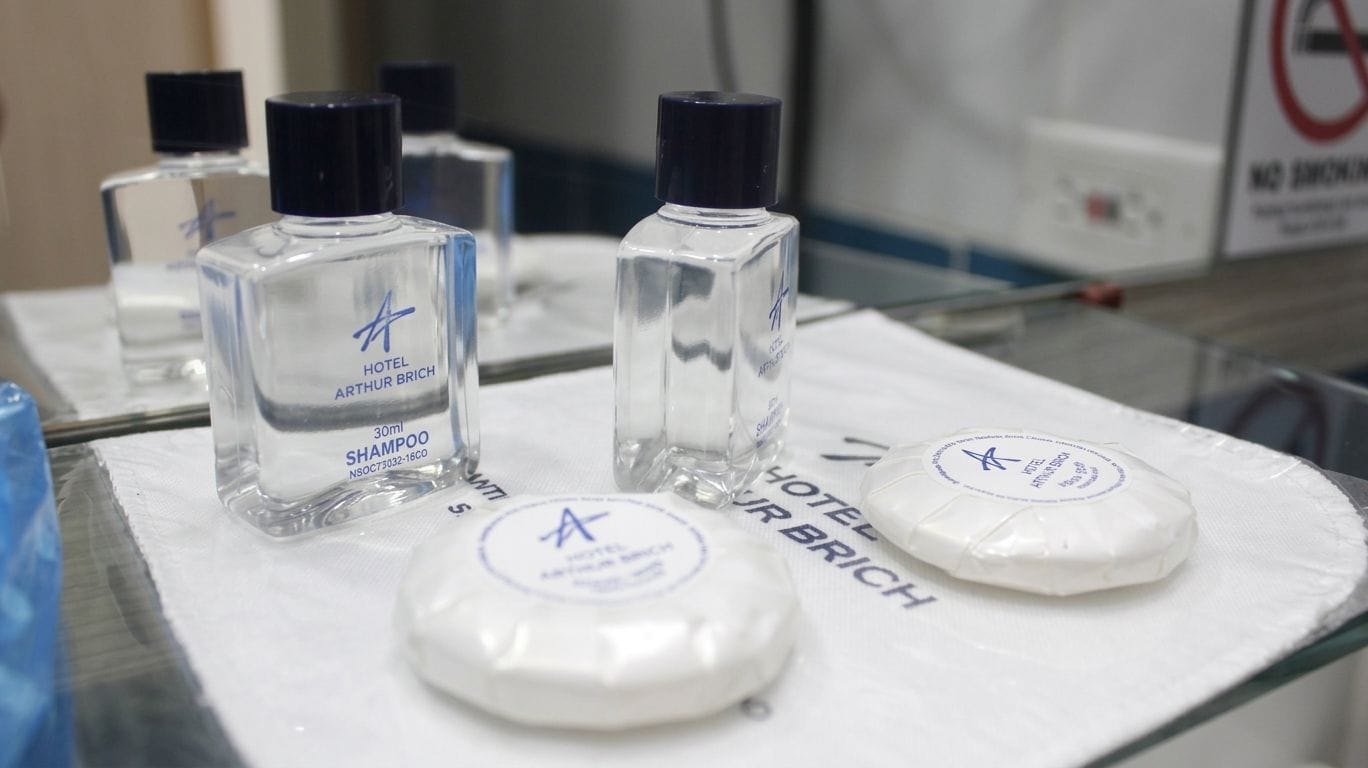 Des articles de toilette d’hôtel sont posés sur un comptoir, notamment un flacon de shampoing et deux savons.