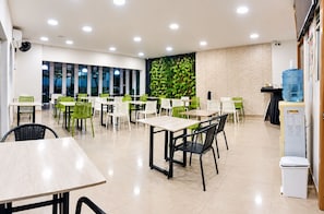 Un comedor moderno con varias mesas y sillas, un dispensador de agua y una pared con una planta verde.