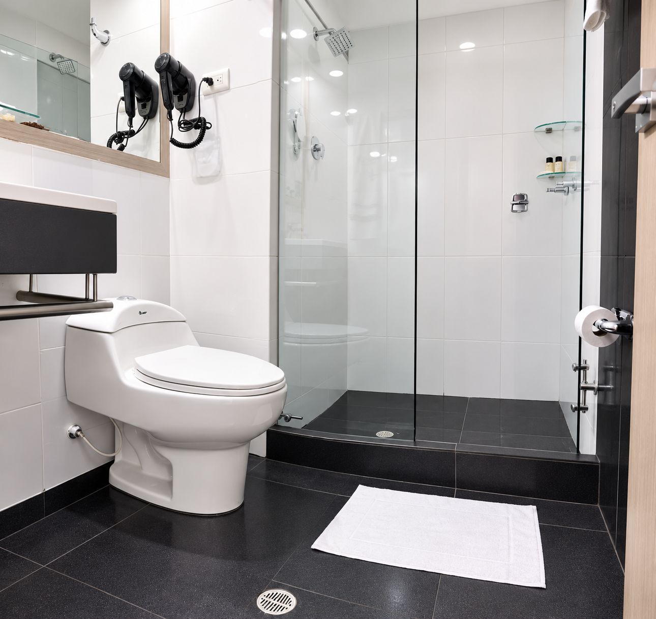Un baño moderno con inodoro, cabina de ducha de vidrio y tocador con espejo.