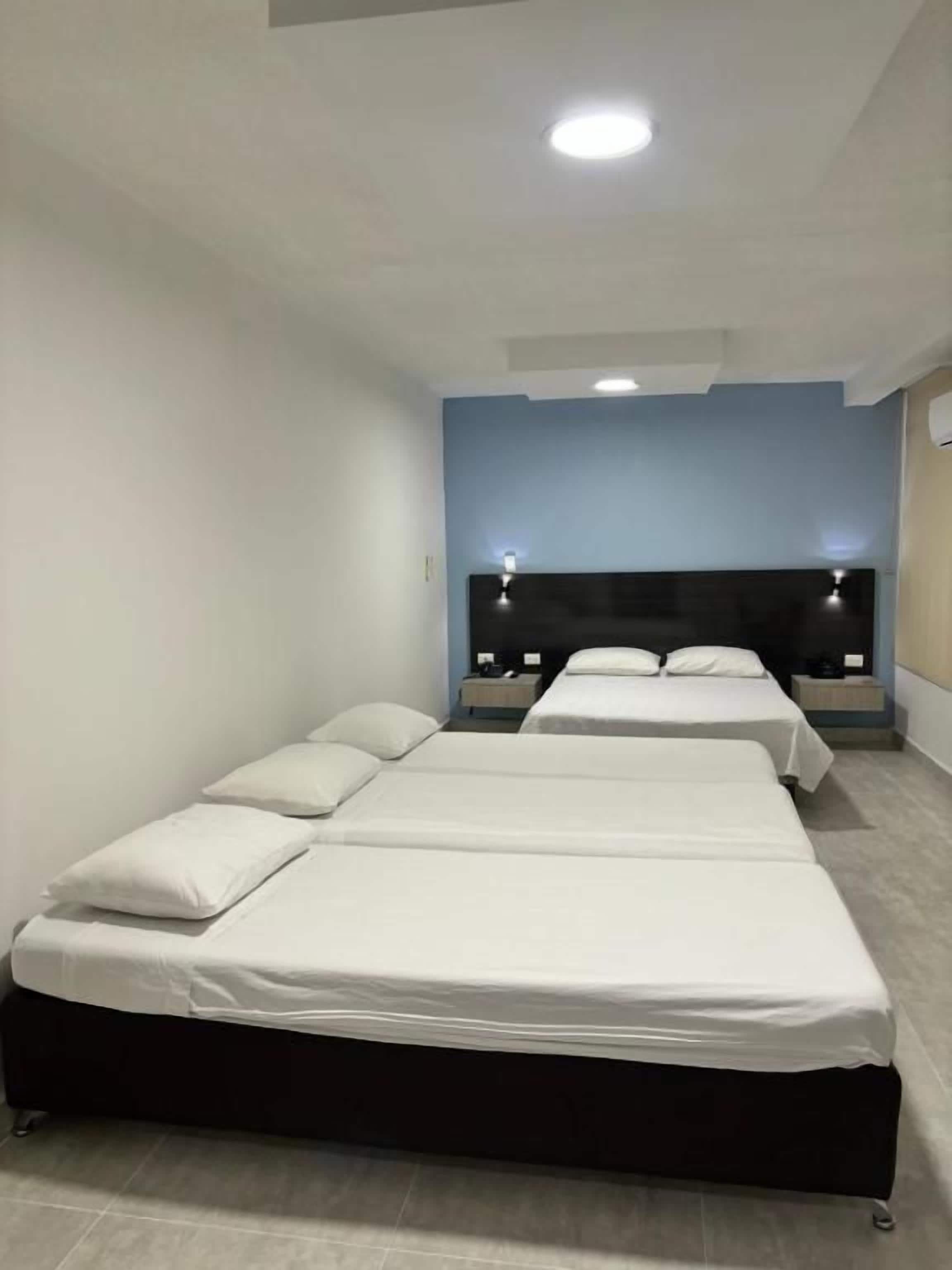 A hotel room with three beds, a dark headboard, and a light-colored floor.